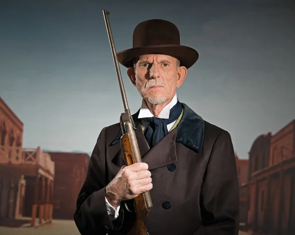Senior western man wearing a brown hat and coat holding rifle. S