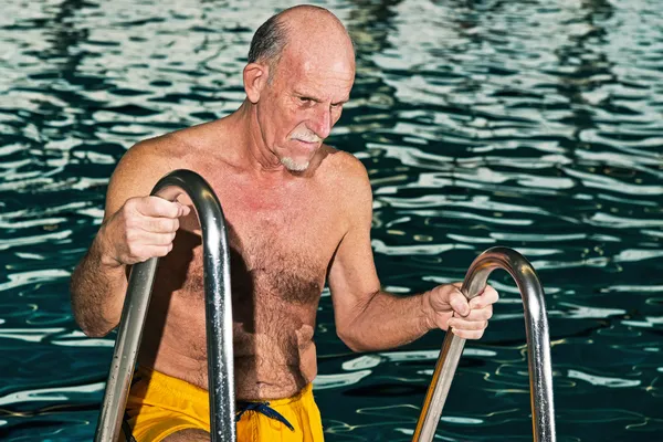 Senior man walking out of swimming pool. Wearing yellow swimming