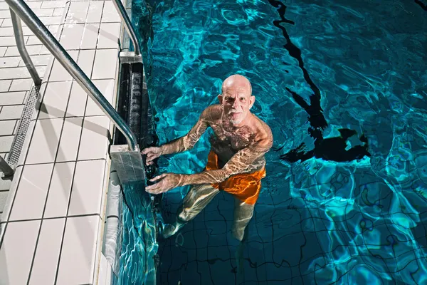 Healthy active senior man with beard in indoor swimming pool. We