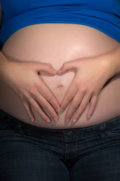Pregnancy belly with hands of mom creating a heart shape. Close-