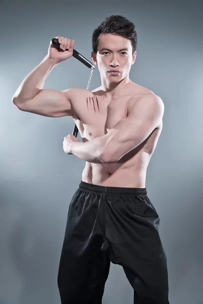 Muscled asian kung fu man in action pose with nunchucks. Blood s