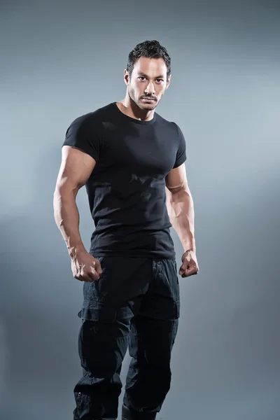 Combat muscled fitness man wearing black shirt and pants. Studio