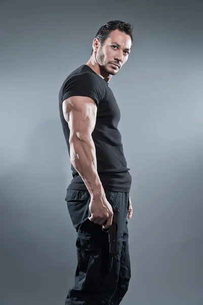 Action hero muscled man holding a gun. Wearing black t-shirt and