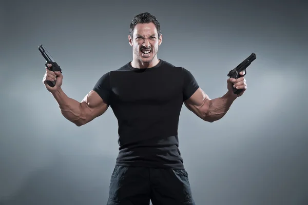 Action hero muscled man holding two guns. Wearing black t-shirt