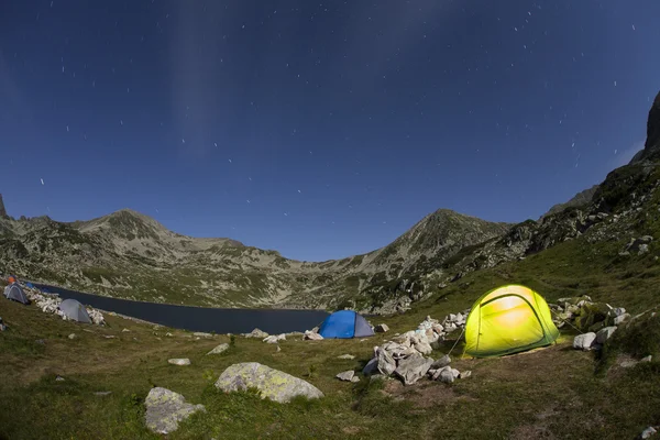 An illuminated tent at night on a camp near to a lake in mountai