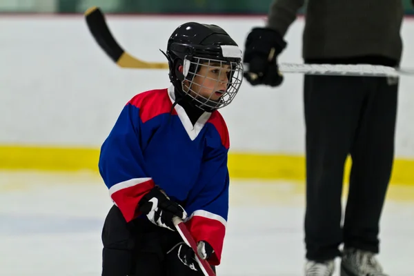 Child ice hockey player at practice with coach watching on
