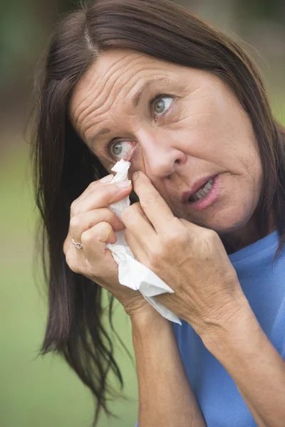 Sad mature woman tissue cleaning tears in eye