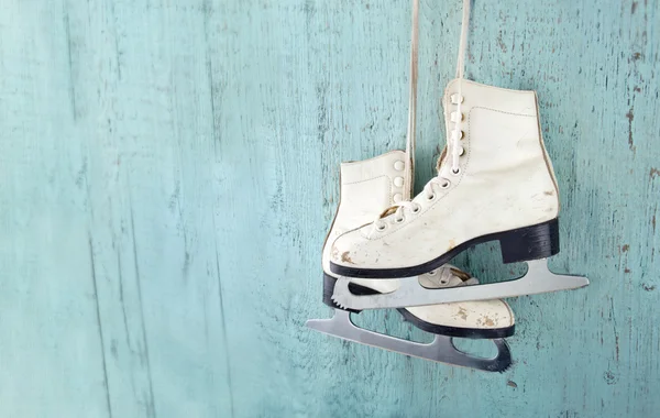 Women\'s ice skates hanging on blue wooden background