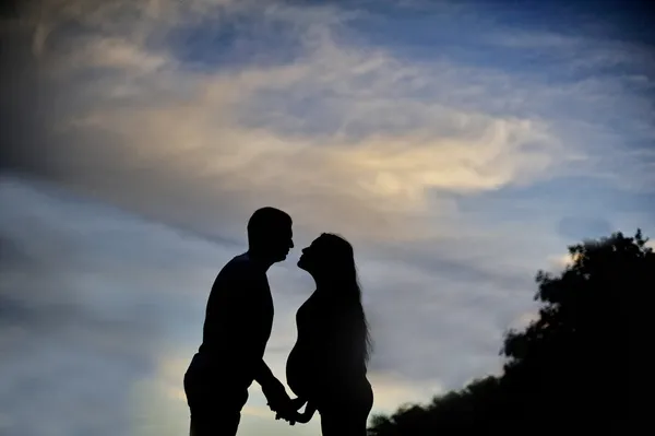 A young man and his pregnant wife at sunset. silhouettes