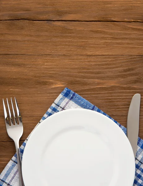 White plate, knife and fork on wood