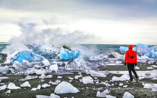 Woman watching waves crash against icebergs at Jokulsarlon glacial lagoon, Iceland