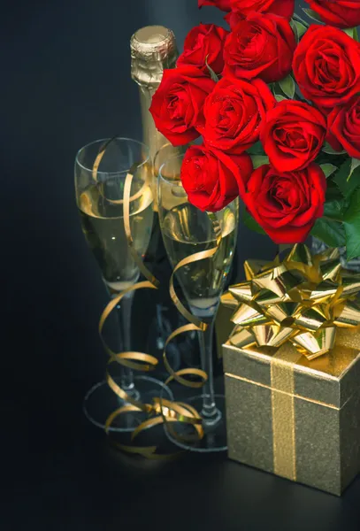 Red roses, golden gift box and and champagne on black background