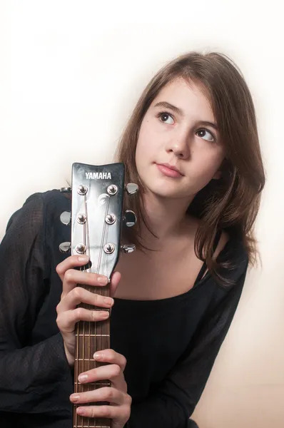 Young brunette teen girl playing acoustic guitar on white