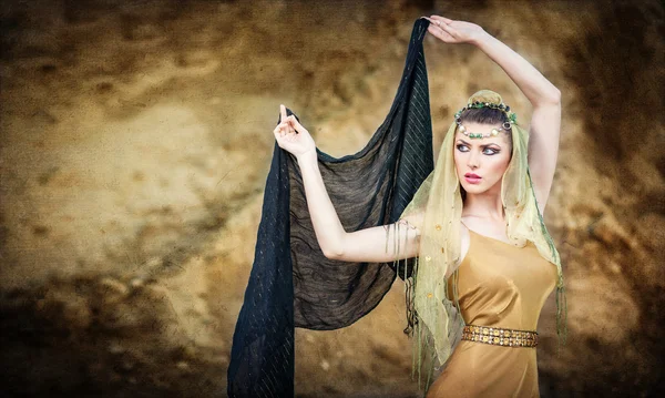 Woman belly dancer with veil against rock beach. Dancing beautiful slim girl. Sexy arabian turkish oriental professional artist in yellow costume and diamond jewelry outdoor. exotic belly-dance star.