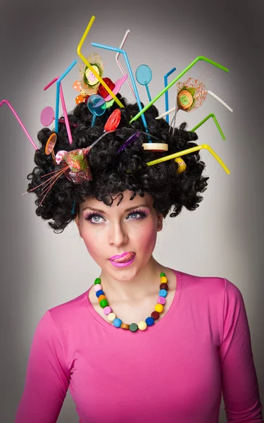 Portrait of a beautiful female model on white background with lollipops in the hair.Glamorous girl with pink blouse wearing lollipop and straw colored in hair