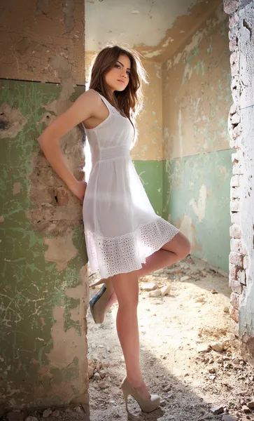 Beautiful girl posing fashion near an old wall. Pretty young woman posing laying on a wall. Very attractive blonde girl with a transparent white short dress. Romantic young woman posing