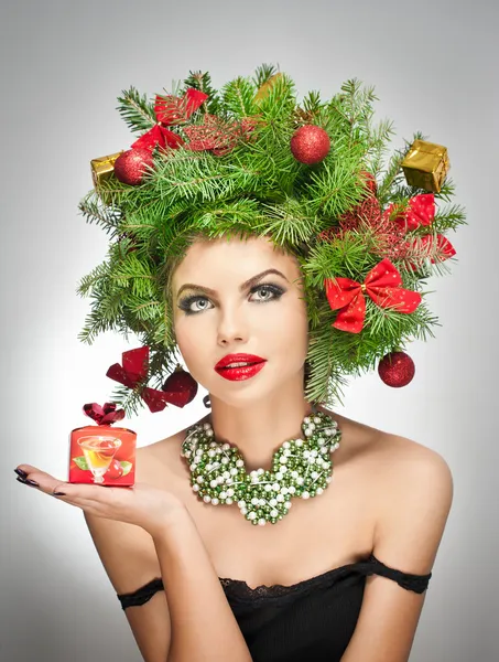 Beautiful creative Xmas makeup and hair style indoor shoot. Beauty Fashion Model Girl. Winter. Beautiful attractive girl with Christmas tree accessories in studio holding a gift.
