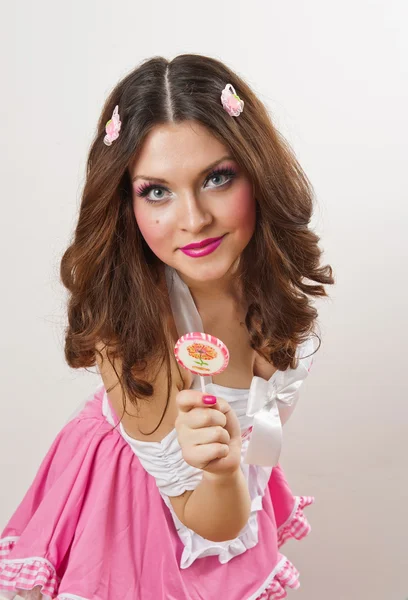 Attractive girl with a lollipop in her hand and pink dress isolated on white. Beautiful long hair brunette playing with a lollipop. Studio shot. Young woman with dynamic look posing pretty