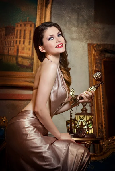 Young beautiful luxurious woman in elegant dress smiling holding a vintage telephone. Beautiful young woman in a luxurious classic interior. Seductive brunette woman in luxury manor, vintage style