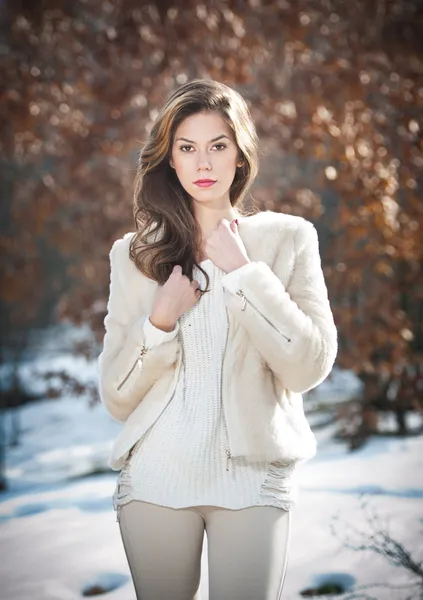 Portrait of young beautiful woman wearing white clothes outdoor. Beautiful brunette girl with long hair posing outdoor in a cold winter day. Beautiful fashionable young woman in winter scenery.