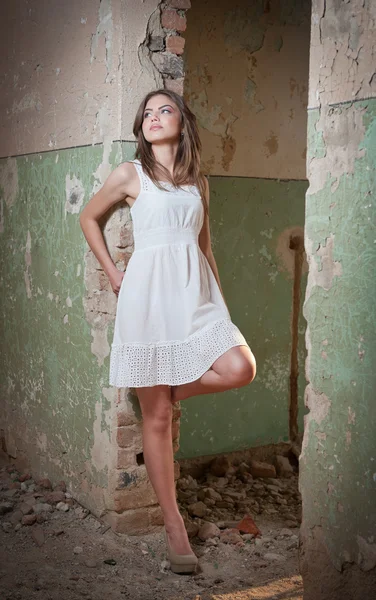 Beautiful girl posing fashion near an old wall. Pretty young woman posing laying on a wall. Very attractive blonde girl with a transparent white short dress. Romantic young woman posing