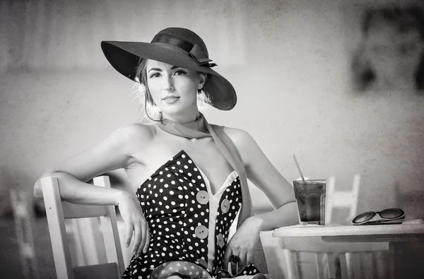 Fashionable attractive lady with hat and scarf sitting in restaurant, indoor shot. Young woman posing in elegant scenery, black and white. Art photo of elegant sensual woman relaxing, vintage style