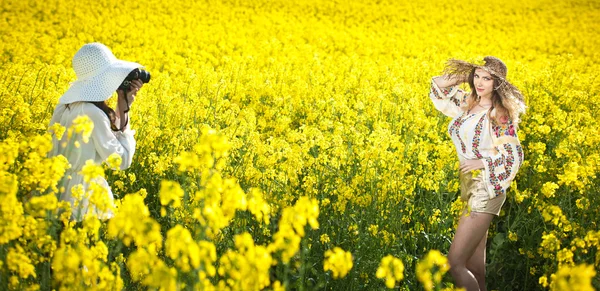 Young girl wearing Romanian traditional blouse and hat posing in canola field, outdoor shot. Lady photographer shooting beautiful blonde smiling and enjoying the bright yellow flowers of rapeseed