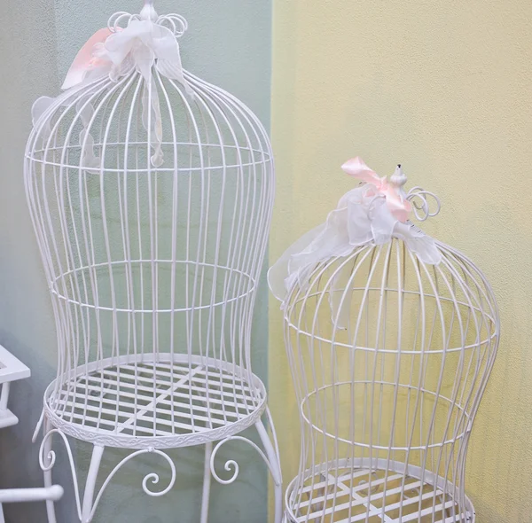Two bird cages with white metal as a symbol of captivity and being trapped or in a confined prison cell. Beautiful decorative cages with pink ribbons. Wedding decoration.