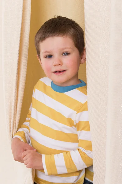 Little boy peeking out from behind the curtains.