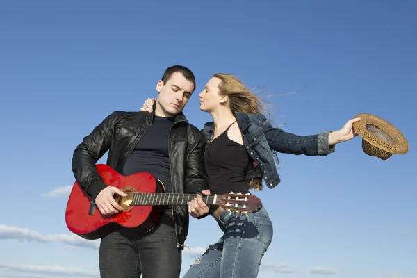 Young beautiful woman with hat in hand and young man playing acoustic guitar