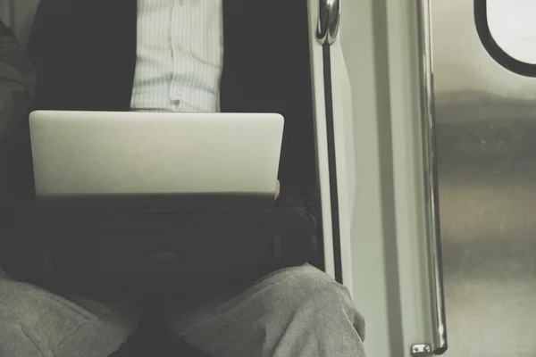 Businessman sitting on seat of train and playing Laptop