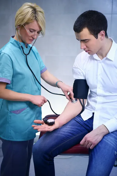 Female doctor checking young man blood pressure
