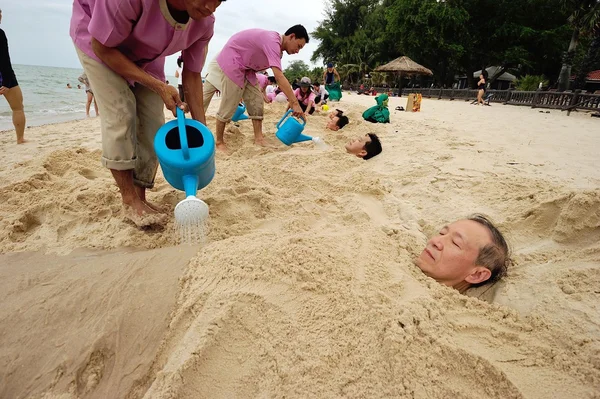 Group of old people buries on the beach for natural therapy in Phetburi , Thailand.