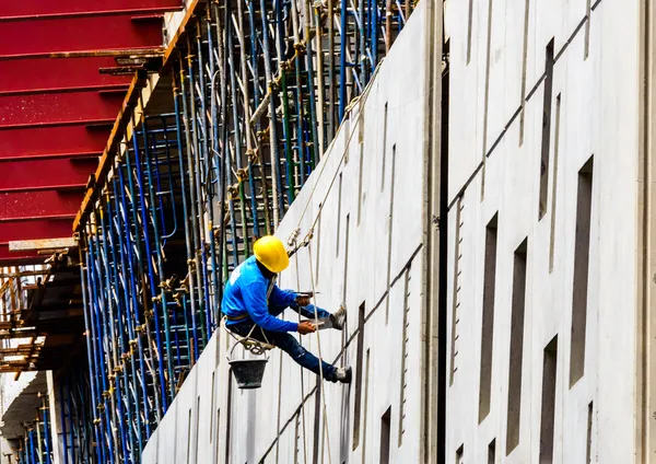 A Construction Workers high up on the wall of a new building.