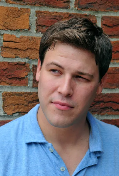 Young male actor making emotional facial expression in front of camera with brick wall background
