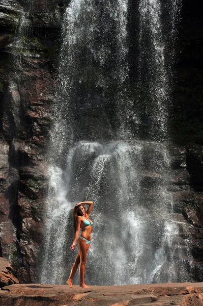 Beautiful slim fitness model posing sexy in front of waterfalls