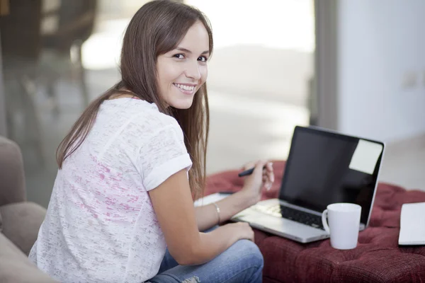 Woman on sofa using a laptop while having cup of tea