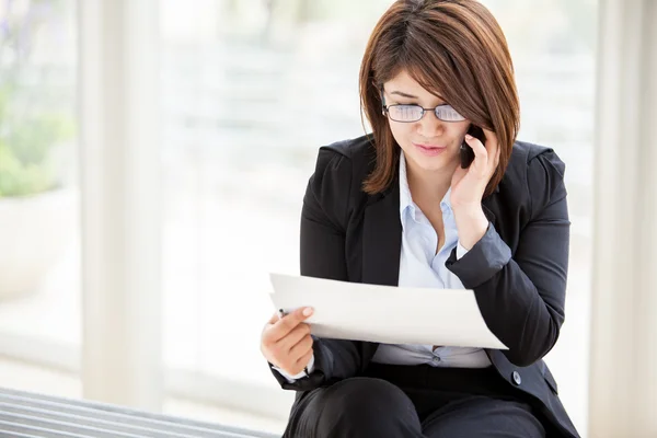 Beautiful business woman looking at papers she holding in her arms while calling on her phone