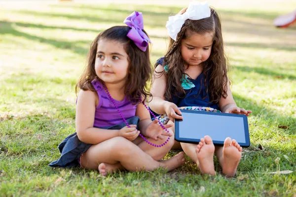 Sweet little cousins using a tablet computer while relaxing at a park