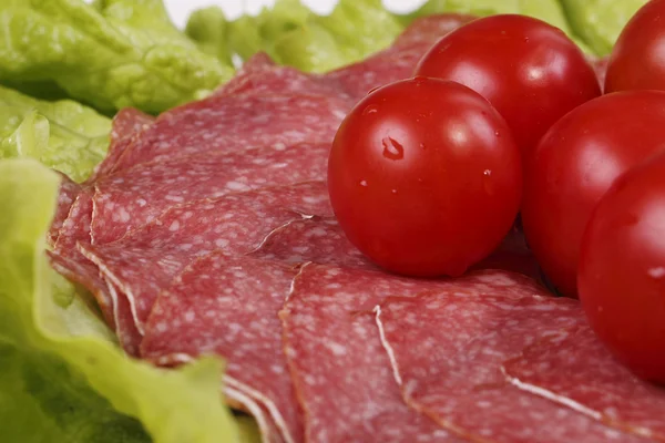 Tomatoes are on thin slices of salami and lettuce