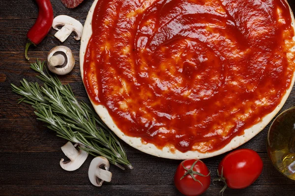 Fresh pizza dough with tomato sauce and natural ingredients for cooking on wooden table