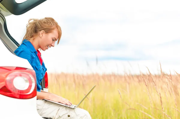 Woman in meadow near car working on laptop. — Stock Photo #14753801