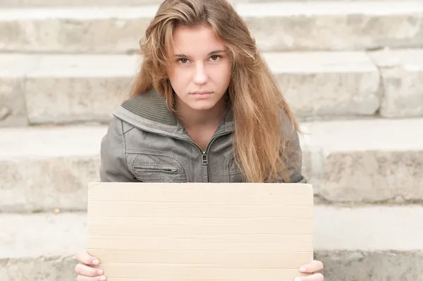 Young sad girl outdoor with blank cardboard sign.
