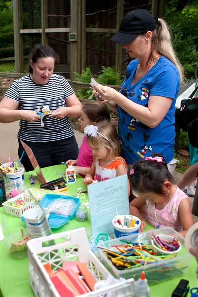 Parents Help Kids With Arts And Crafts Project At Festival