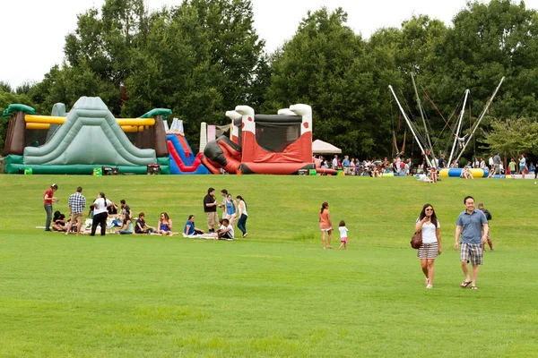 People Enjoy Activities And Relaxing On Grass At Summer Festival