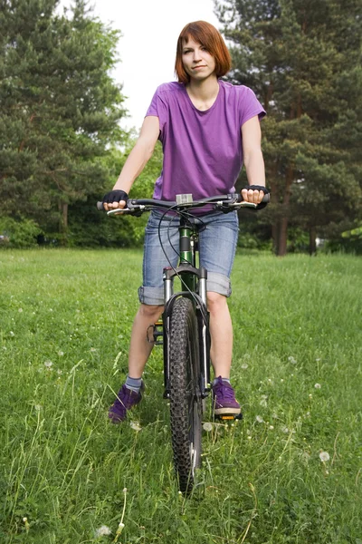 Girl in purple shirt on bicycle in park