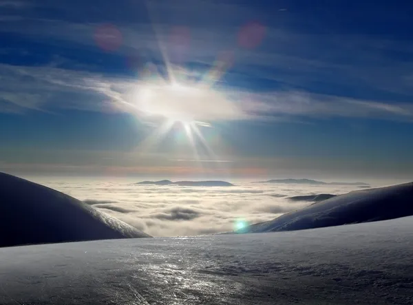 Beautiful winter mountains landscape, over the clouds, opposite to sunset sky
