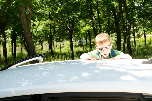 Young blond boy climbing to the rooftop of a car