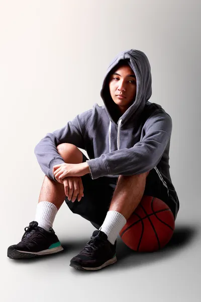 Sad teenager boy sitting on basketball