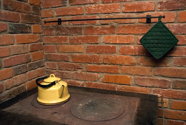 Yellow tea pot on a stove, red brick wall in background